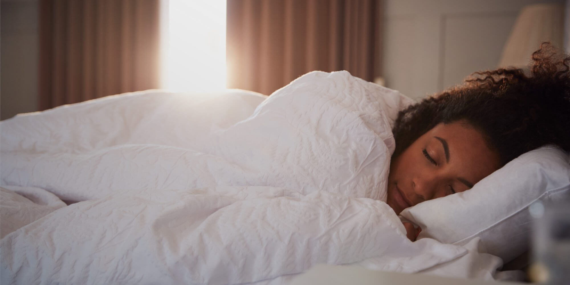 A woman sleeping peacefully in a sunlit bedroom, for the article on sleep hygiene and brain health